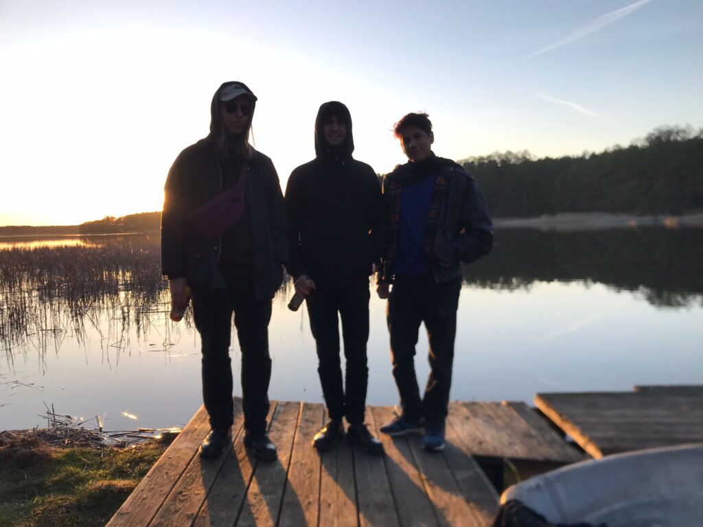 The three Adventure Team members Jonathan, Ian and Juan appearing as silhouettes due to being photographed against the light of the setting sun on the jetty of a lake by Ahlimbsmühle in Brandenburg. Picture by Rachel Horsman. 